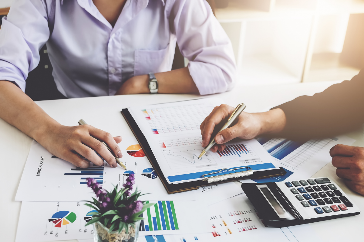 Accountants sit at a desk reviewing report, Pages with charts and a calculator on the desk.